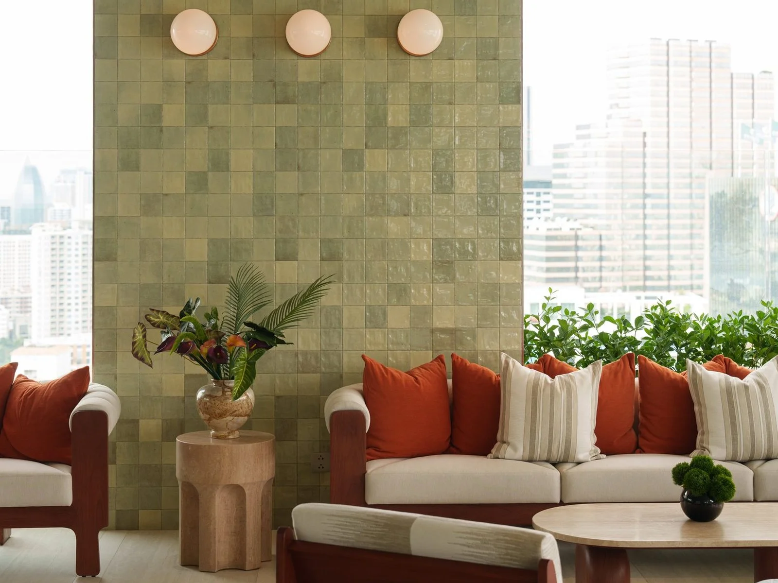 Common lounge area with green tiled wall and orange cushioned sofas at Via Ari, Thailand